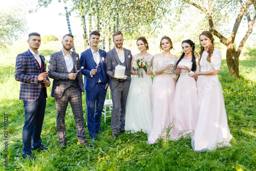 Bride and groom, together with friends, celebrate their wedding with champagne in nature
