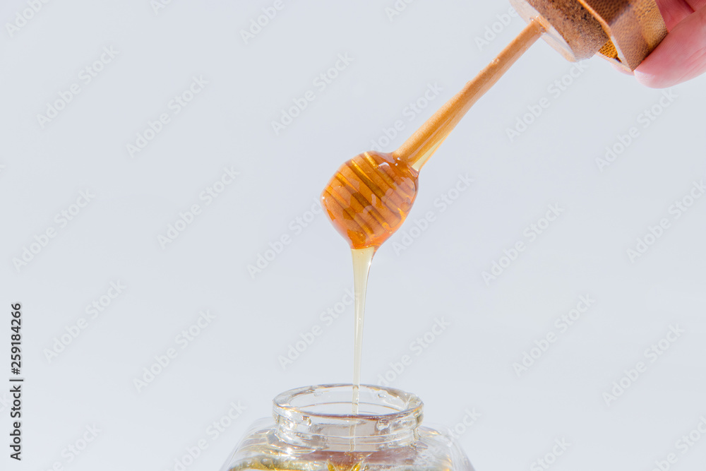Honey dripping from wooden honey dipper on white background Honey dripping from wooden honey dipper on white background