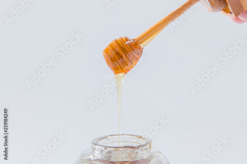 Honey dripping from wooden honey dipper on white background