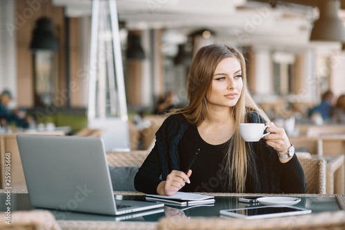 Beautiful girl working out a plan of the project and concept. Girl paints a website design on a laptop. student prints a message on the phone in the messenger. Development. Digital marketing
