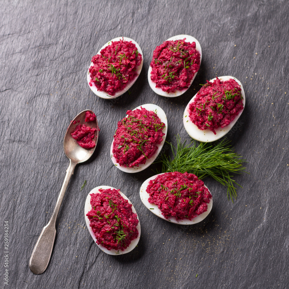 Stuffed eggs with beetroot with cream cheese, garlic and spicy herbs on a black slate background