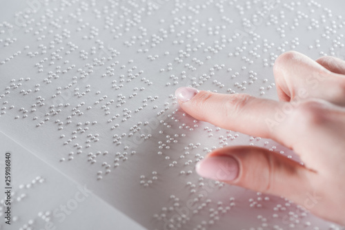 partial view of young woman reading braille text on white paper photo
