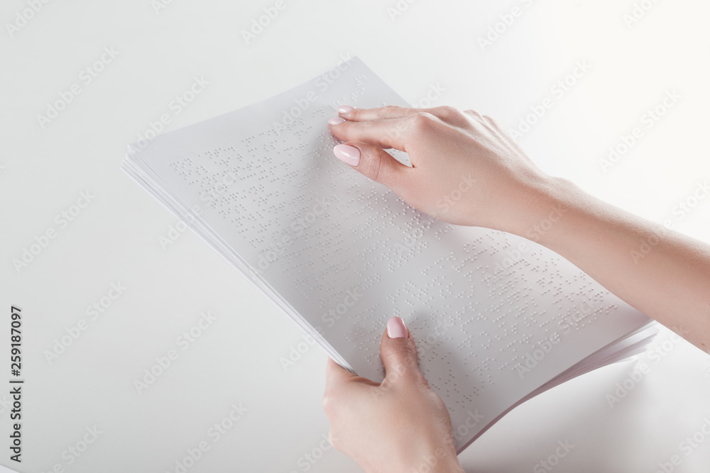 cropped view of young woman reading braille text with hand on white paper cropped view of young woman reading braille text with hand on white paper