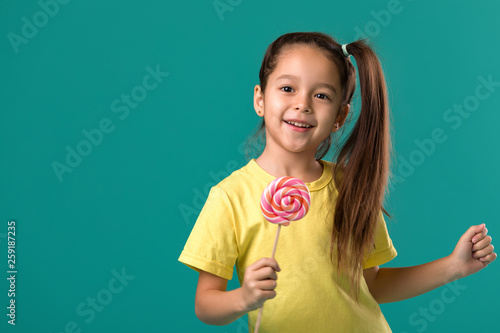 Beautiful cute little child girl with sweet candy lollipop isolated on blue background
