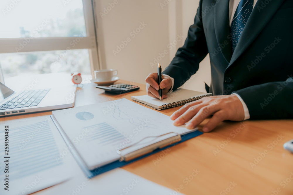 Working process startup. Businessman working at the wood table with new finance project. Modern notebook on table. Pen holding hand Working process startup. Businessman working at the wood table with new finance project. Modern notebook on table. Pen holding hand