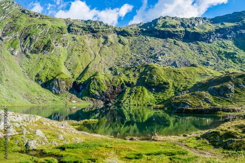 Balea lake near Transfagarasan road in the Carpathian Mountains, Romania, Eastern Europe. Green meadows and water in the wilderness on a summer day. Vacation and travel destination.  © Theodor Negru