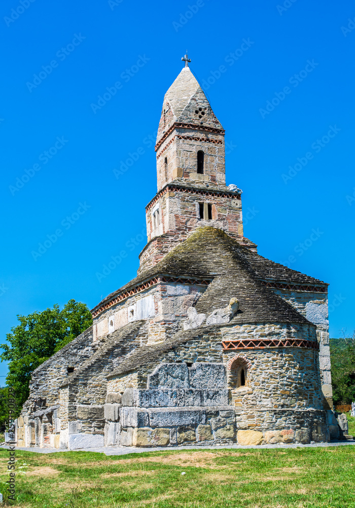 Medieval Densus church in a sunny summer day with blue sky and green grass. Historic monument and one of the oldest church in Romania, Transylvania, Eastern Europe.