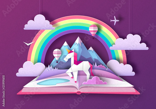 Open fairy tale book with unicorn, rainbow and mountain landscape. Cut out paper art style design © annbozhko