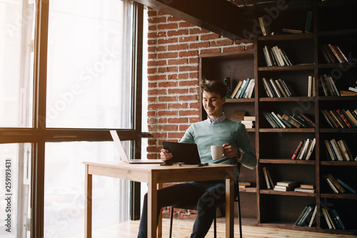 Young handsome student typing on his notebook his diploma. Student discussing on the phone universities's timetable. Education online. Work on freelance. Software development.