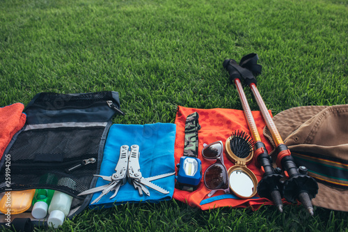 Set of equipment for hiking and travel on green grass with copy space . Items include trekking pole, multi tool, flashlight, hygiene products, tracking clothes, sleeping bag