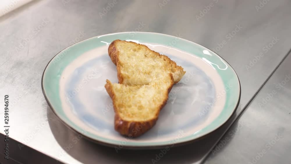 A close-up of chefs hands in black gloves putting halves of cut roasted croissant onto a plate A close-up of chefs hands in black gloves putting halves of cut roasted croissant onto a plate