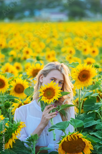 Beautiful young woman with long blonde hair is covered her face to sunflower