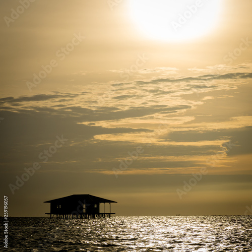 A silhouette of Traditional floating cottage that abandoned by residents of Harapan Island, Indonesia with beautiful orange sky