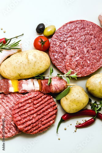 different types of raw meat: chicken thighs, pork and beef burgers, ribs and kebabs, turkey meatballs, ready to be cooked with potatoes, hot pepper, olives and black olives . Meat Food Background