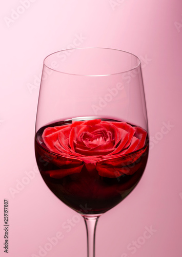Wine with rose in glass against pink background