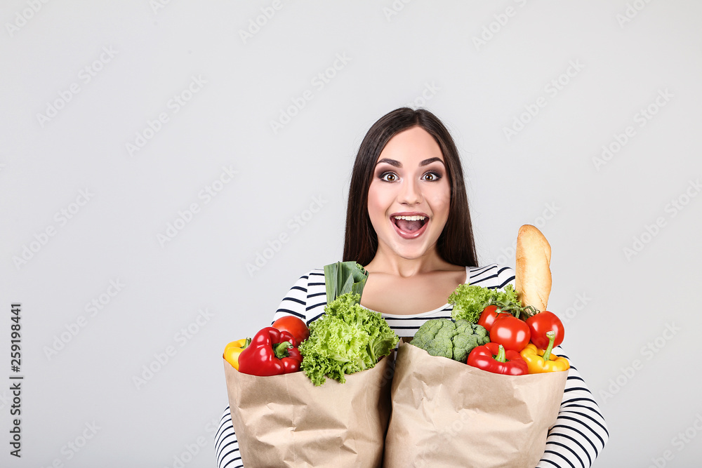 Beautiful woman holding grocery shopping bags on grey background Beautiful woman holding grocery shopping bags on grey background