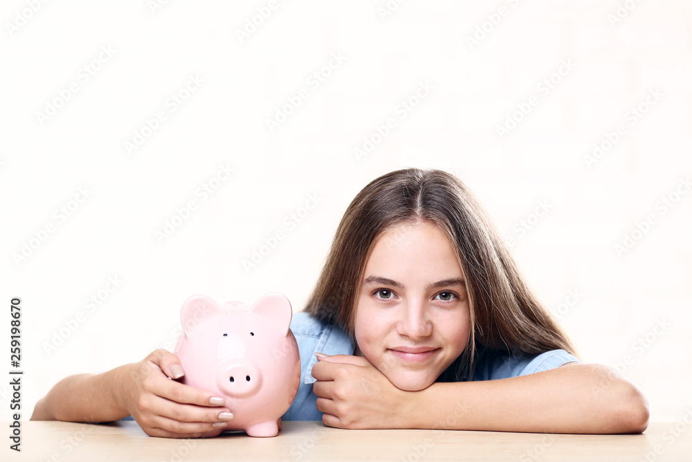 Young girl with pink piggybank sitting at table Young girl with pink piggybank sitting at table