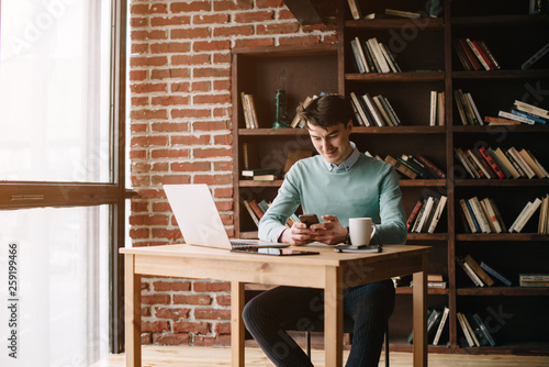 Young handsome student typing on his notebook his diploma. Student discussing on the phone universities's timetable. Education online. Work on freelance. Software development.