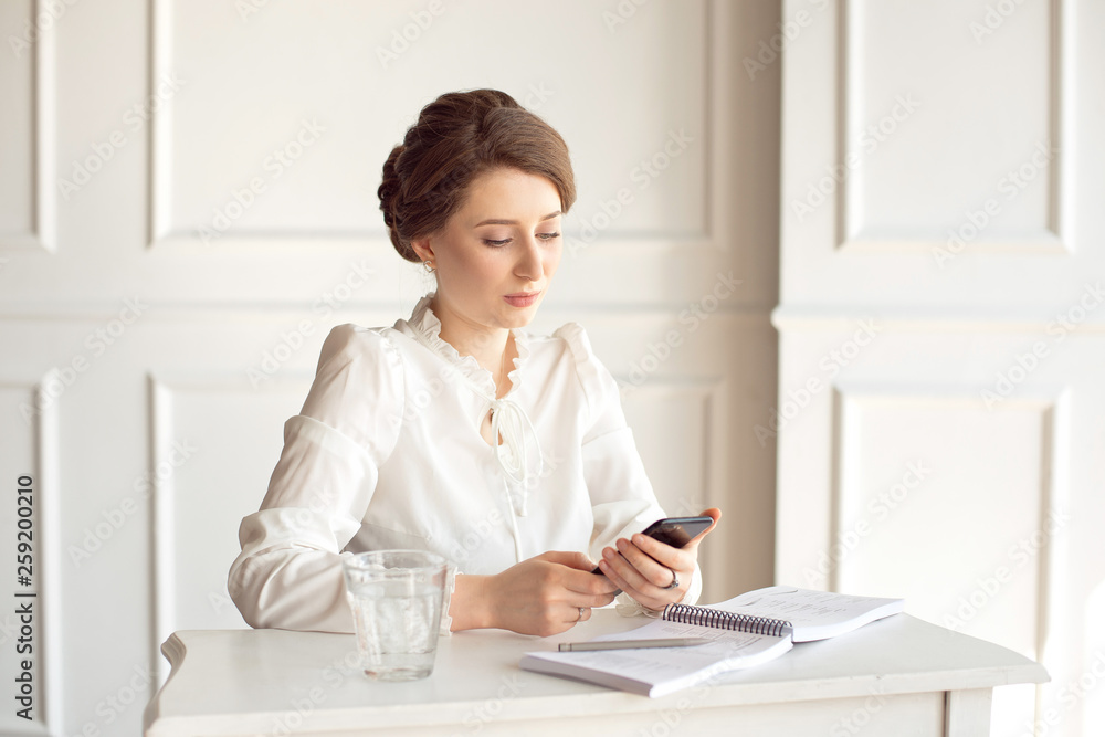 Portrait of a beautiful smiling young brunette businesswoman in a white shirt sitting on a bright modern workstation working with papers . Portrait of a beautiful smiling young brunette businesswoman in a white shirt sitting on a bright modern workstation working with papers .