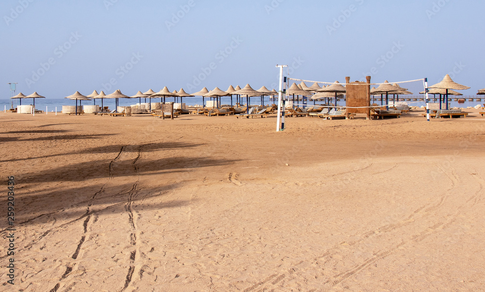 Obraz premium deserted , abandoned beach with footprints in the sand, sunbeds, umbrellas and a volleyball net overlooking the sea