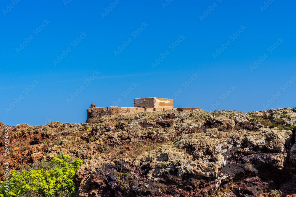 Spain, Lanzarote, Ancient castle santa barbara behind colorful volcanic rock