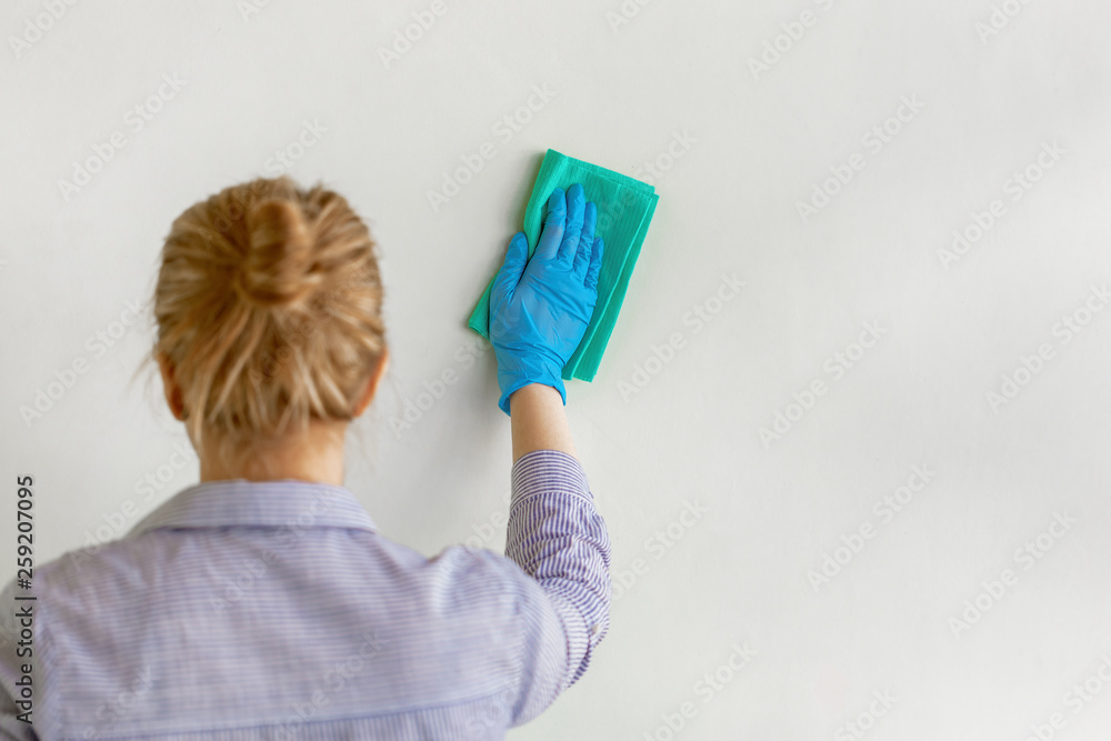 Employee hand in blue rubber protective glove wiping wall from dust with dry rag. Commercial cleaning company. Employee hand in blue rubber protective glove wiping wall from dust with dry rag. Commercial cleaning company.