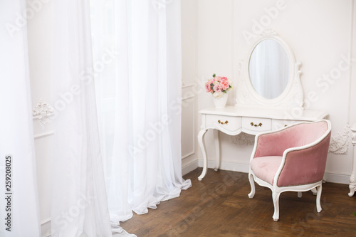 Royal bedroom. Boudoir room with pink soft armchair. Elegant white dressing table in light classic luxury interior