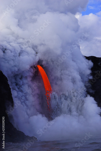 Hot lava flows from high cliff into the ocean in Big Island in Hawaii