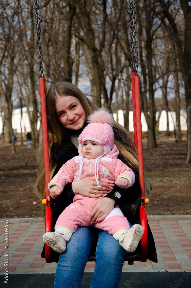 Mom plays on a bright playground with a small child in the street, nomads, a house during the day Mom plays on a bright playground with a small child in the street, nomads, a house during the day
