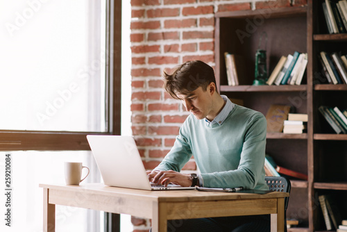 Young handsome student typing on his notebook his diploma. Student discussing on the phone universities's timetable. Education online. Work on freelance. Software development.