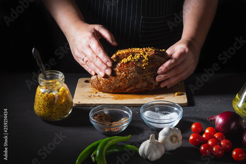 Preparation of the Female chef the fried beef for roast beef on black wooden table, hands, close up. To smear of mustard.