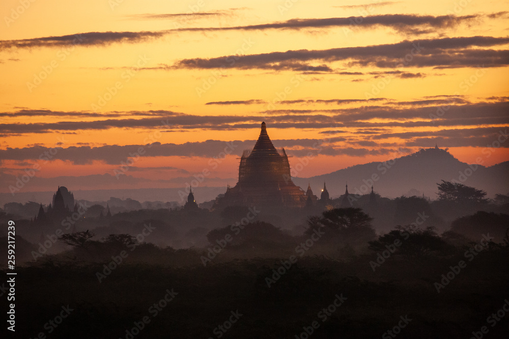 Beautiful sunrise over the ancient pagodas in Bagan, Myanmar. Orange sky and fog between the hills