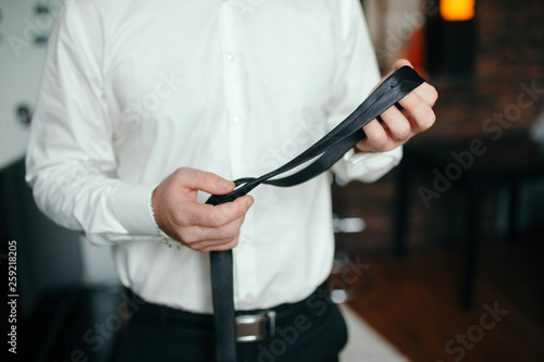 People, business,fashion and clothing concept - close up of man in shirt dressing up and adjusting tie on neck at home.