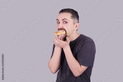Man with a beard eating a bun over gray background