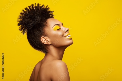 Excitement African American Fashion Model profile portrait . Satisfied Brunette young woman with afro hair style,creative yellow make up, lips and eyeshadows on colorful background photo