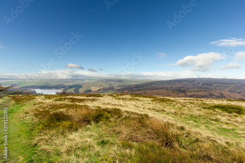 A view of a lake in a valley with green grass slopes under a majestic blue sky and white clouds