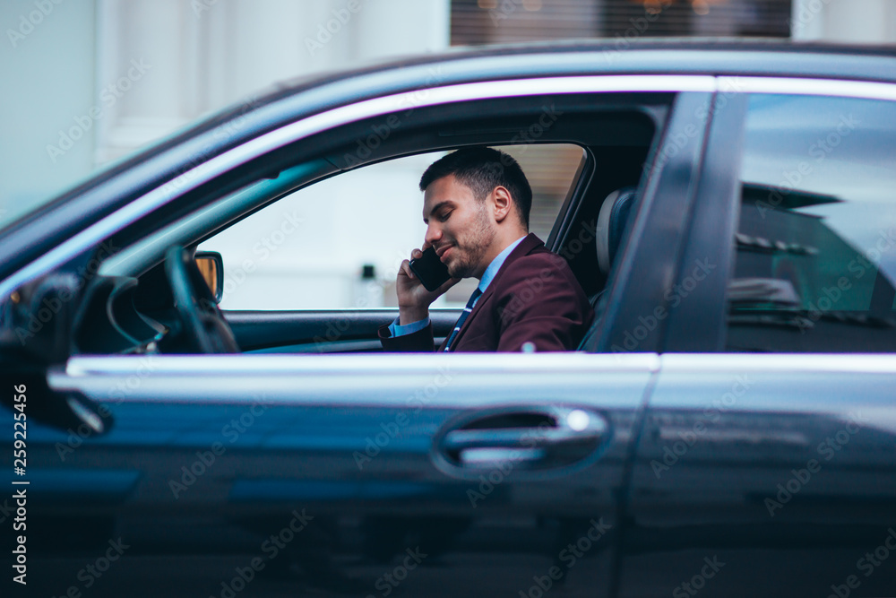 A manager sitting at the front seat of his limo talking on his cellphone while making a lot of hand gestures.