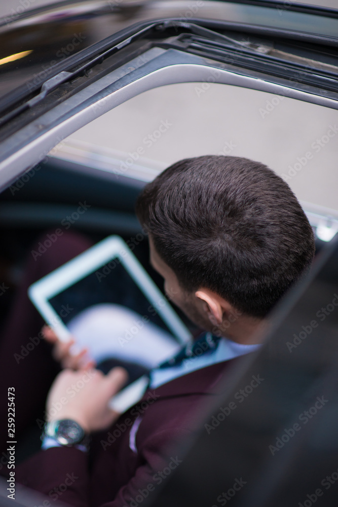 Above head perspective of a businessman working on his tablet while sitting in his black limo. Above head perspective of a businessman working on his tablet while sitting in his black limo.