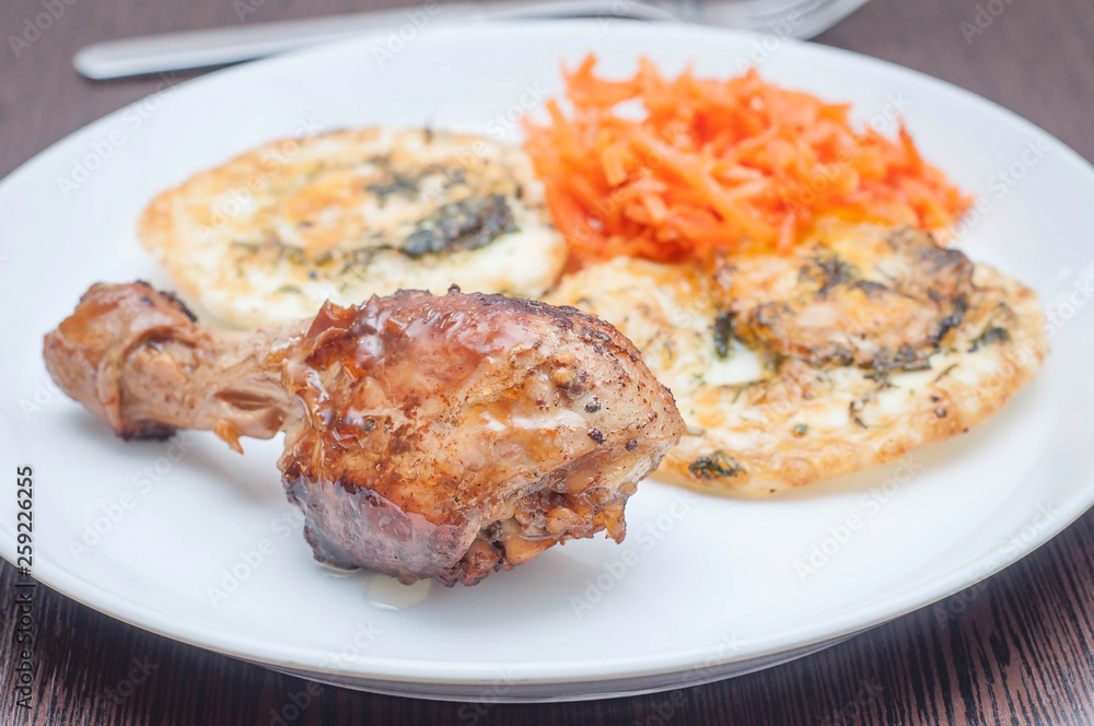 Morning avtrak for nasiyeniya useful substances. Fried chicken leg on the background of fried eggs and Korean carrots on a white plate on a wooden table.