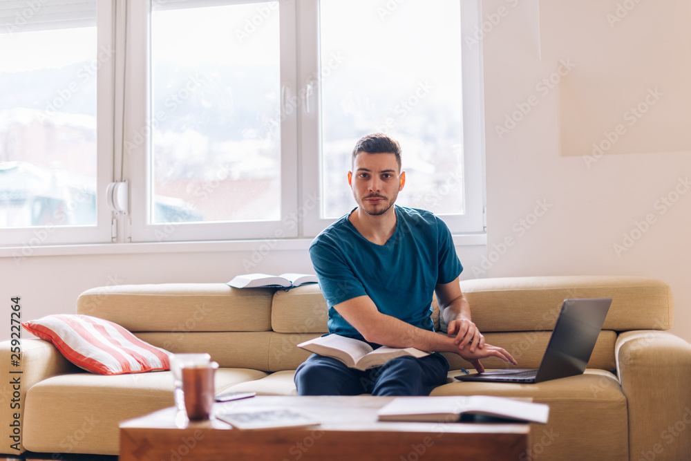 Handsome student studying on the couch with few opened books and a laptop next to him. Handsome student studying on the couch with few opened books and a laptop next to him.