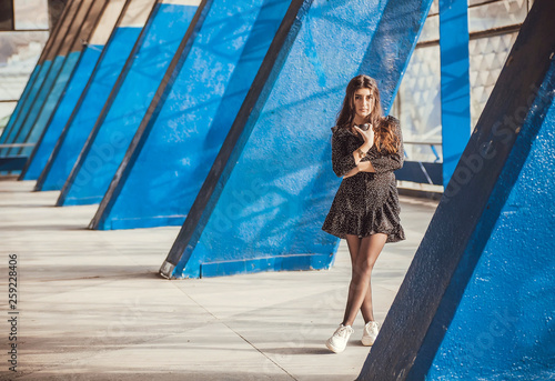 Lonely beautiful girl standing between blue columns of grunge city area. Young woman drinking coffee in urban sunny space photo