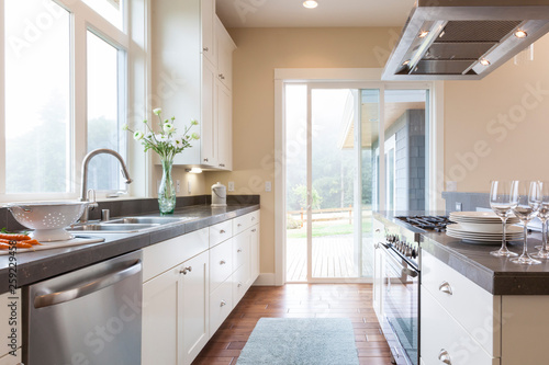 Light, bright, contemporary upscale home kitchen interior with laminate cabinets, stone countertops, stainless steel appliances, big windows and sliding glass doors.