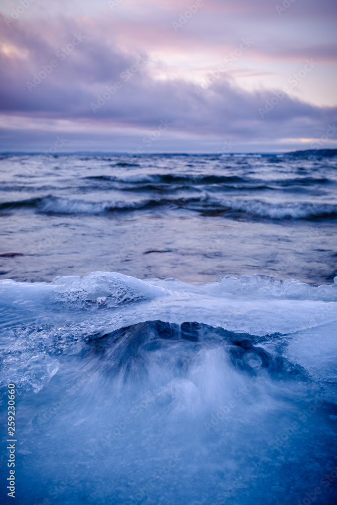 wave flushes on an icy beach colorful clouds in the background