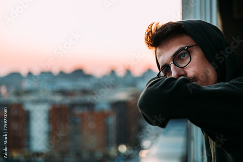 Portrait of a young man looking at sunset from a balcony thinking about life