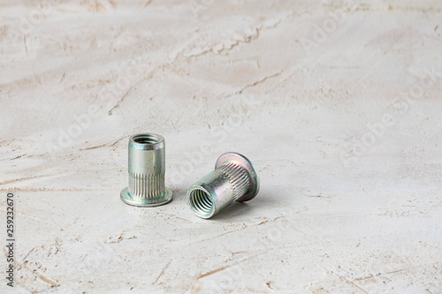 Two metal grey river nuts for hard internal thread for thin units on left part of oblong horizontal shot textured cement background with copy space photo