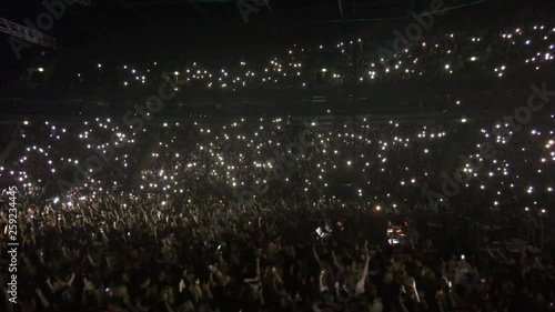 Crowd of people with turned on the lights on concert at the ballad playing. Fans waving arms with mobile phone light