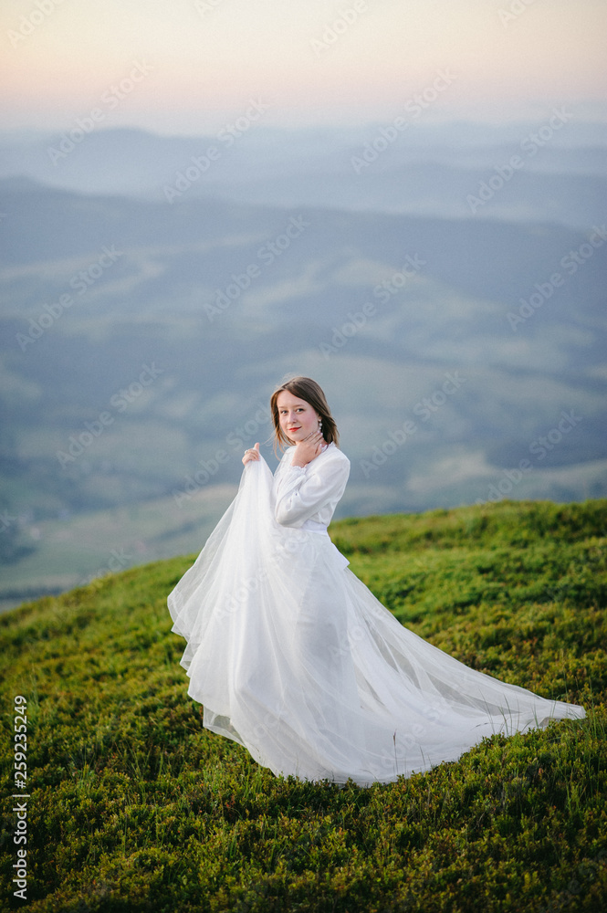 woman in a wedding dress runs across the field toward the mountains