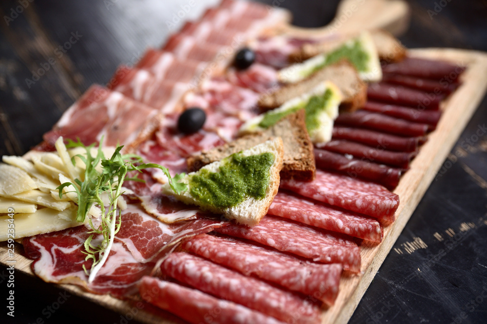 slicing of sausage and meat with croutons and olives on a wooden board