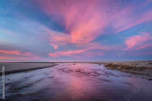 Pink clouds and blue sky over the fast river on the sandy beach at sunset