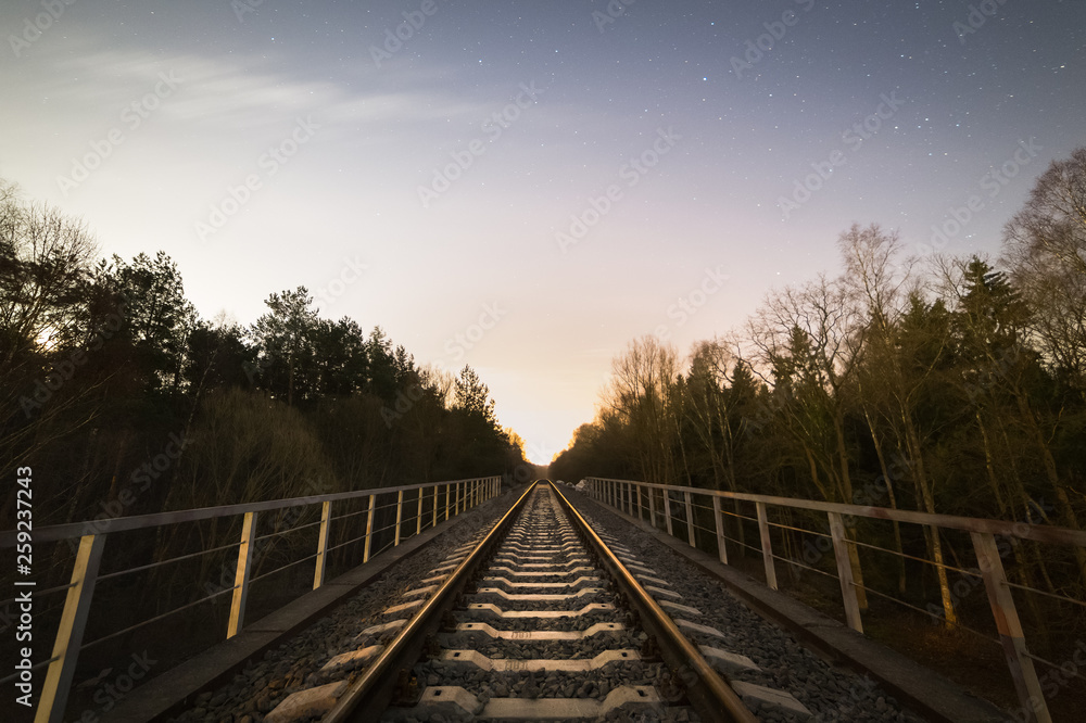 Fototapeta premium Railway track in the forest at cold starry night